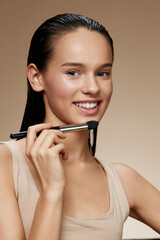 Young female model with a natural look applying makeup with a brush, showcasing a healthy beauty...