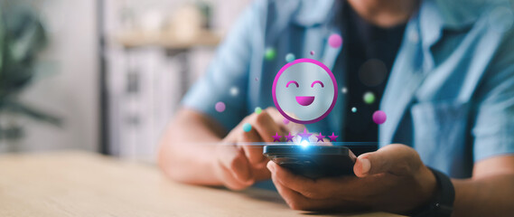 Close-up of hand using smartphone with glowing happy face and five-star rating icon. Concept of...