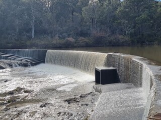 The Douglass Weir on the Wingecarribee River near Berrima New South Wales Australia. The weir is overflowing in a small cascade. The banks of the river lined with Australian gum trees.