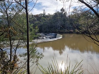 The Douglass Weir on the Wingecarribee River near Berrima New South Wales Australia. The weir is overflowing in a small cascade. The banks of the river lined with Australian gum trees.