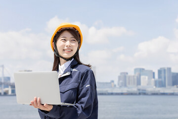 ノートパソコンを使う作業服を着た若い女性