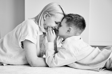 Little son showing love to his mom. Young mother and her kid lying on white carpet and spending...