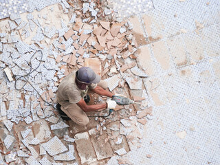 Dedicated construction worker removing old tile floor with power tool for home renovation project...