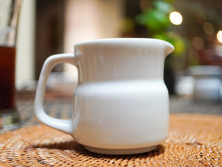 Elegant white ceramic creamer pitcher resting on woven placemat in warm inviting breakfast setting