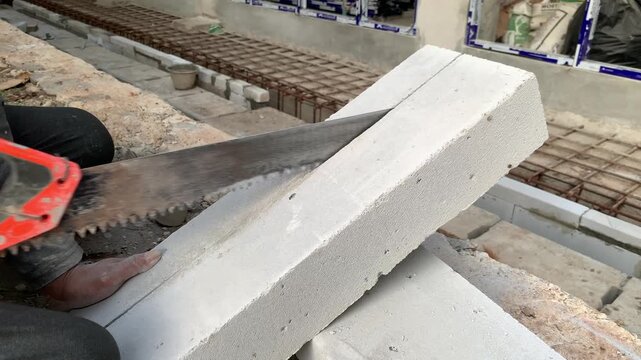 Hands of construction worker or handyman is cutting lightweight bricks or hebel using a saw. The process of breaking lightweight bricks that will be used to make the walls of a building
