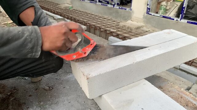 Hands of construction worker or handyman is cutting lightweight bricks or hebel using a saw. The process of breaking lightweight bricks that will be used to make the walls of a building
