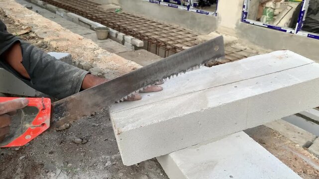 Hands of construction worker or handyman is cutting lightweight bricks or hebel using a saw. The process of breaking lightweight bricks that will be used to make the walls of a building