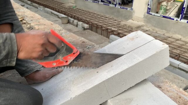 Hands of construction worker or handyman is cutting lightweight bricks or hebel using a saw. The process of breaking lightweight bricks that will be used to make the walls of a building