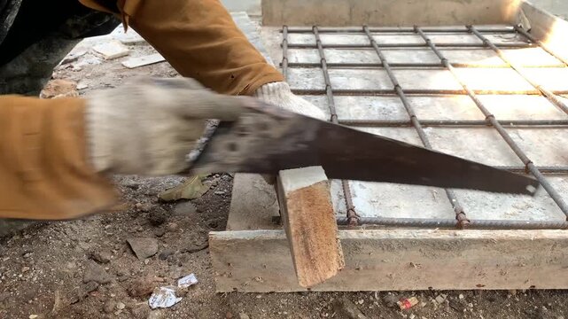 Hands of construction worker or handyman that wearing gloves is cutting wood on the formwork using saws
