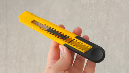 A stationery knife in a woman's hand on a gray background. Retractable utility knife