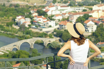 A woman, photographed from behind, stands on a viewpoint over city of Trebinje, Bosnia and...
