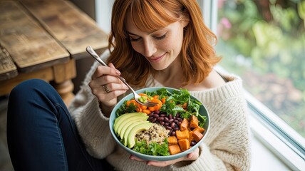 Happy young woman enjoying a fresh healthy vegan salad bowl indoors with natural light and a focus on nourishment