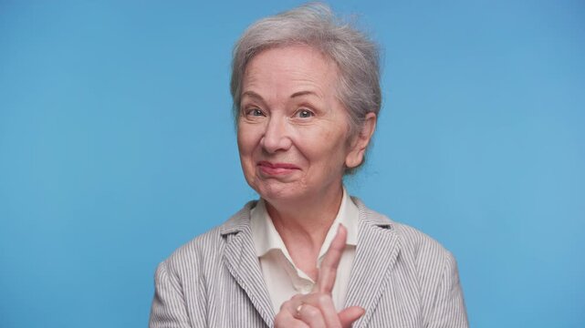 Playful senior woman giving a warning gesture on blue