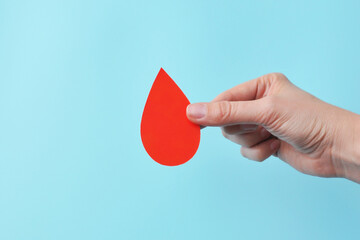 Hand offering a red blood drop on a blue backdrop, symbolizing donation and healthcare.