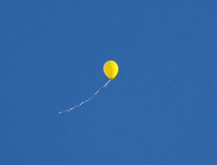 A yellow balloon flying in the air against a blue sky background