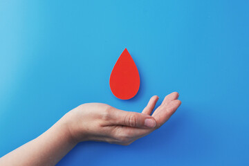 Hand offering a red blood drop on a blue backdrop, symbolizing donation and healthcare.