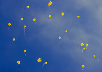 Several yellow balloons rising in the air against a blue sky