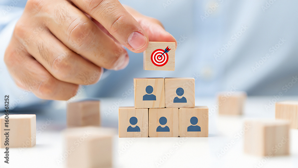 Poster hand placing target block on top of team blocks in pyramid formation on a white surface table top