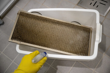 Cleaning dirty kitchen range hood grease filter with spray bottle and rubber gloves