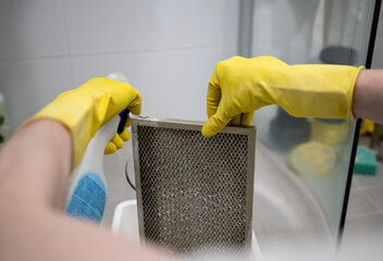 Cleaning dirty kitchen range hood grease filter with spray bottle and rubber gloves