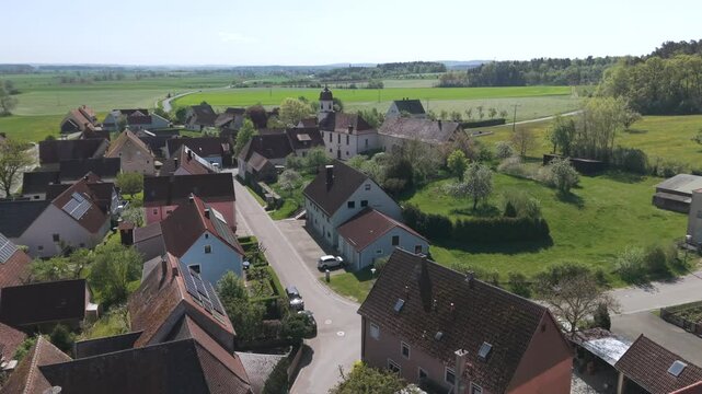A drone fly over during Spring across a small Franconia village called Thann nearby Ansbach embedded in green landscape and and a small river