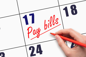 17th day of the month.  Hand writing Pay bills reminder and drawing a line on calendar with red pen...