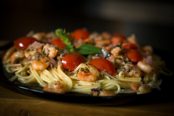 ready to eat and served on a black plate - noodles with shrimp, cherry tomatoes and fresh herbs out...