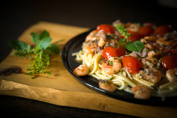ready to eat and served on a black plate - noodles with shrimp, cherry tomatoes and fresh herbs out the garden