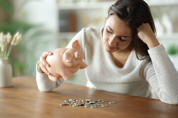 Frustrated woman checking money from piggy bank