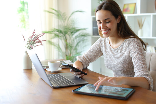 Happy woman using multiple devices on a table at home