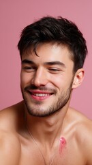Naklejka premium Young Man With Lipstick Stains Smiling Cheerfully Against a Soft Pink Background