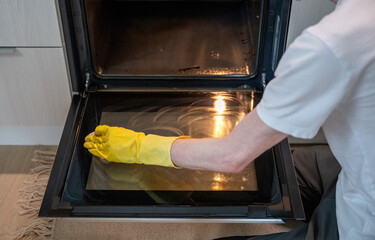 Person cleaning oven door glass with sponge with yellow rubber gloves