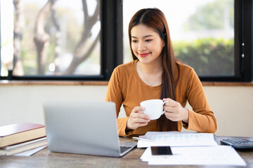 Young woman in casual holding cup use laptop computer drinking coffee sit alone at table in home...