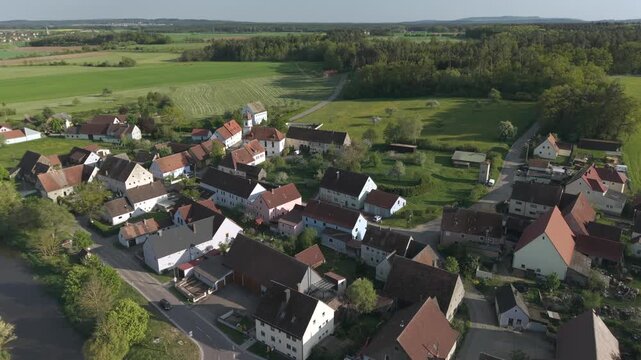 A drone fly over during Spring across a small Franconia village called Thann nearby Ansbach embedded in green landscape and and a small river
