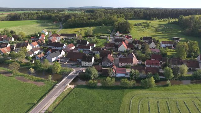 A drone fly over during Spring across a small Franconia village called Thann nearby Ansbach embedded in green landscape and and a small river