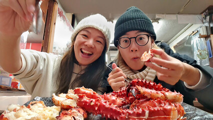 Young lesbian couple enjoying crab feast at local Sankaku Market, Hokkaido, Japan — king crab, snow crab seafood market. Backpacking culture, self-guided travel