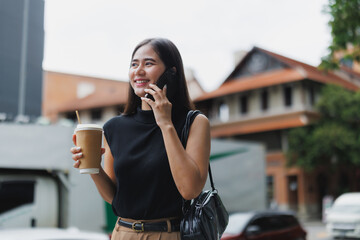 Smiling businesswoman walking in city, talking on phone and holding coffee