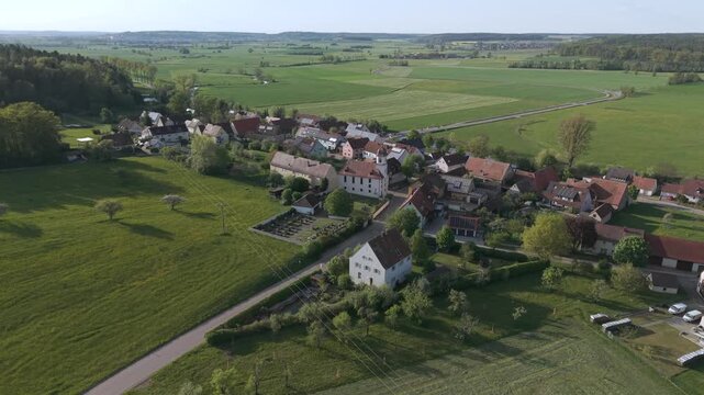 A drone fly over during Spring across a small Franconia village called Thann nearby Ansbach embedded in green landscape and and a small river