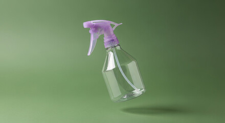 Empty plastic spray bottle with a purple trigger levitating on a solid green background