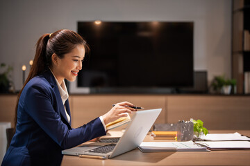 Young Business Woman Taking Notes lookoing at Laptop Computer Sitting At Desk In Modern Office.