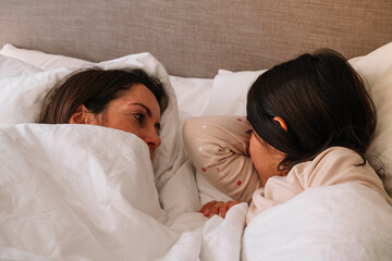 Two women are sleeping in a bed with one of them having her head under the other. Scene is peaceful and intimate
