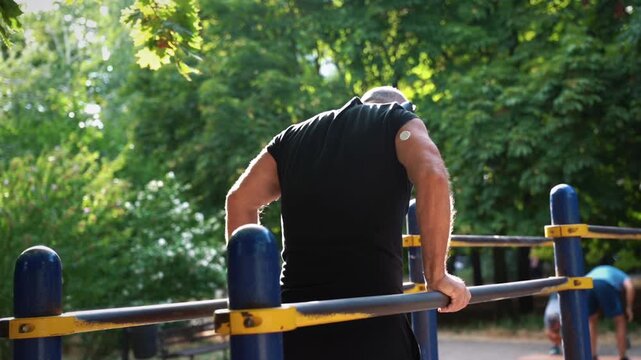 Man with glucose monitoring sensor doing push-ups on parallel bars
