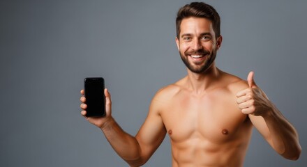 Fototapeta premium Smiling man holding a smartphone while giving a thumbs-up against a gray background