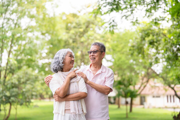 Fototapeta premium Happy smiling senior couple family hugging while walking in summer city park enjoying retirement and spending time together in nature. Romance, love. care and elderly people relationship concept.