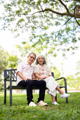 Elderly couple sitting on a bench in spring or summer park. Old man and woman outdoors, life in...