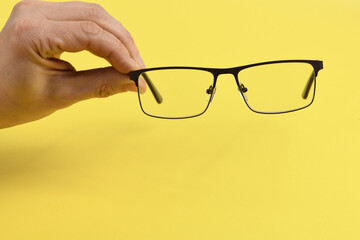 Hand holding plastic black glasses, isolated on yellow background.
