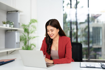 Focused asian business woman using laptop in modern office, looking at screen, chatting, reading or...