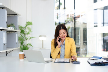 Young businesswoman cheerful asian lady in suits working in office, sitting by workdesk with...