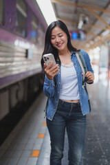 Young tourist using smartphone while waiting for train at station