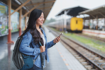 Young woman using smartphone while waiting for train at station